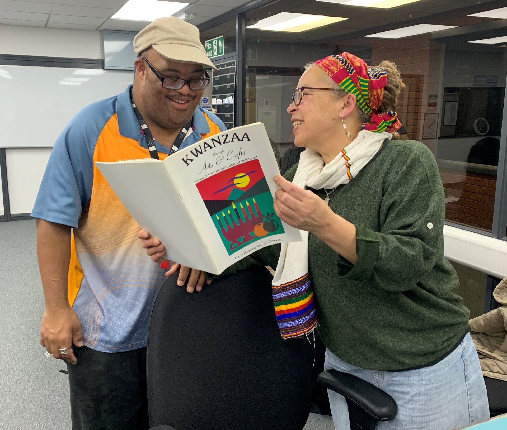 A man reading a book being held open by a lady. She looks at the man smiling.