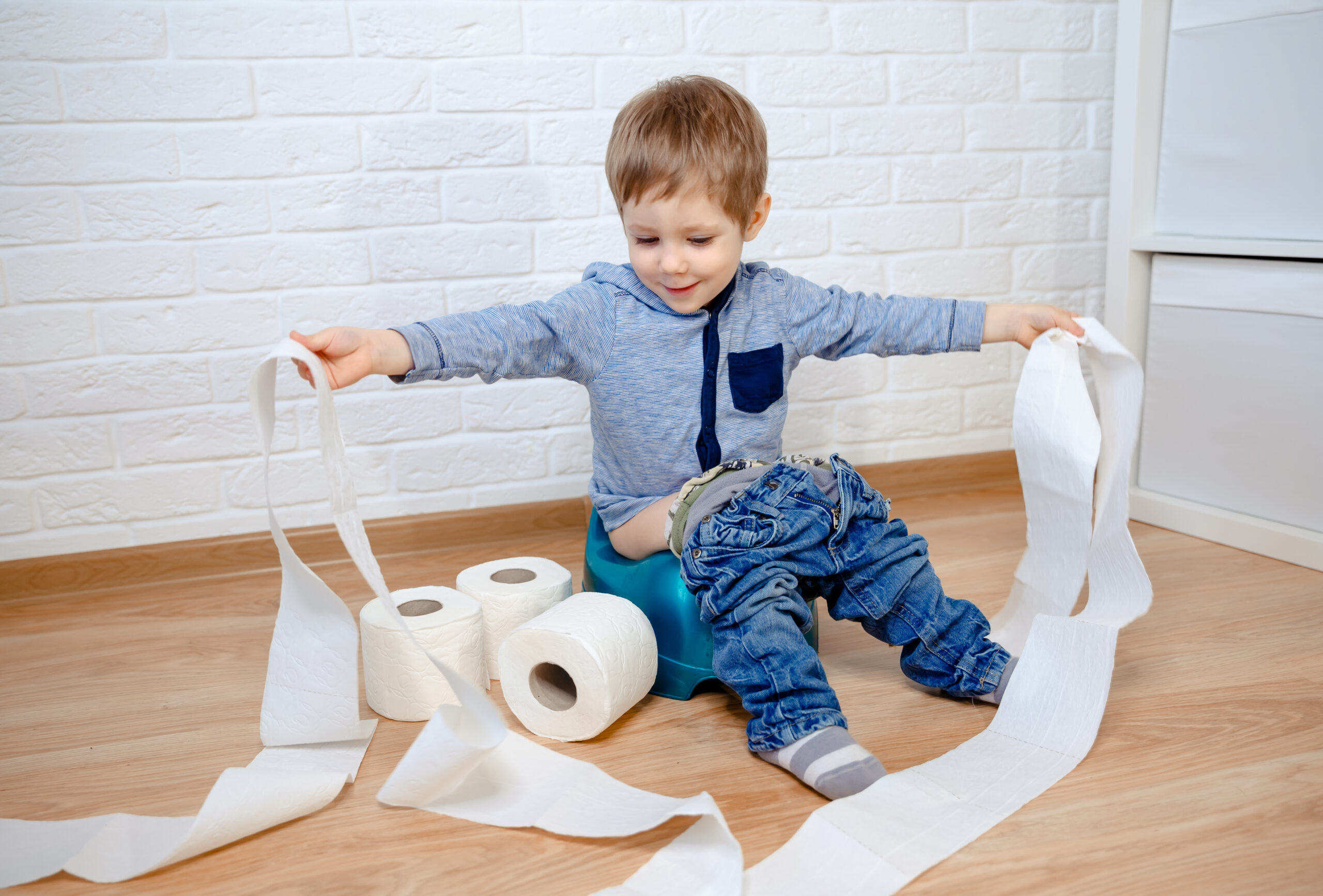 A young boy sat on a potty playing with toilet roll.