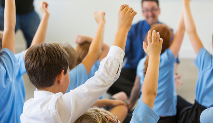 School children raising their hand in a classroom.