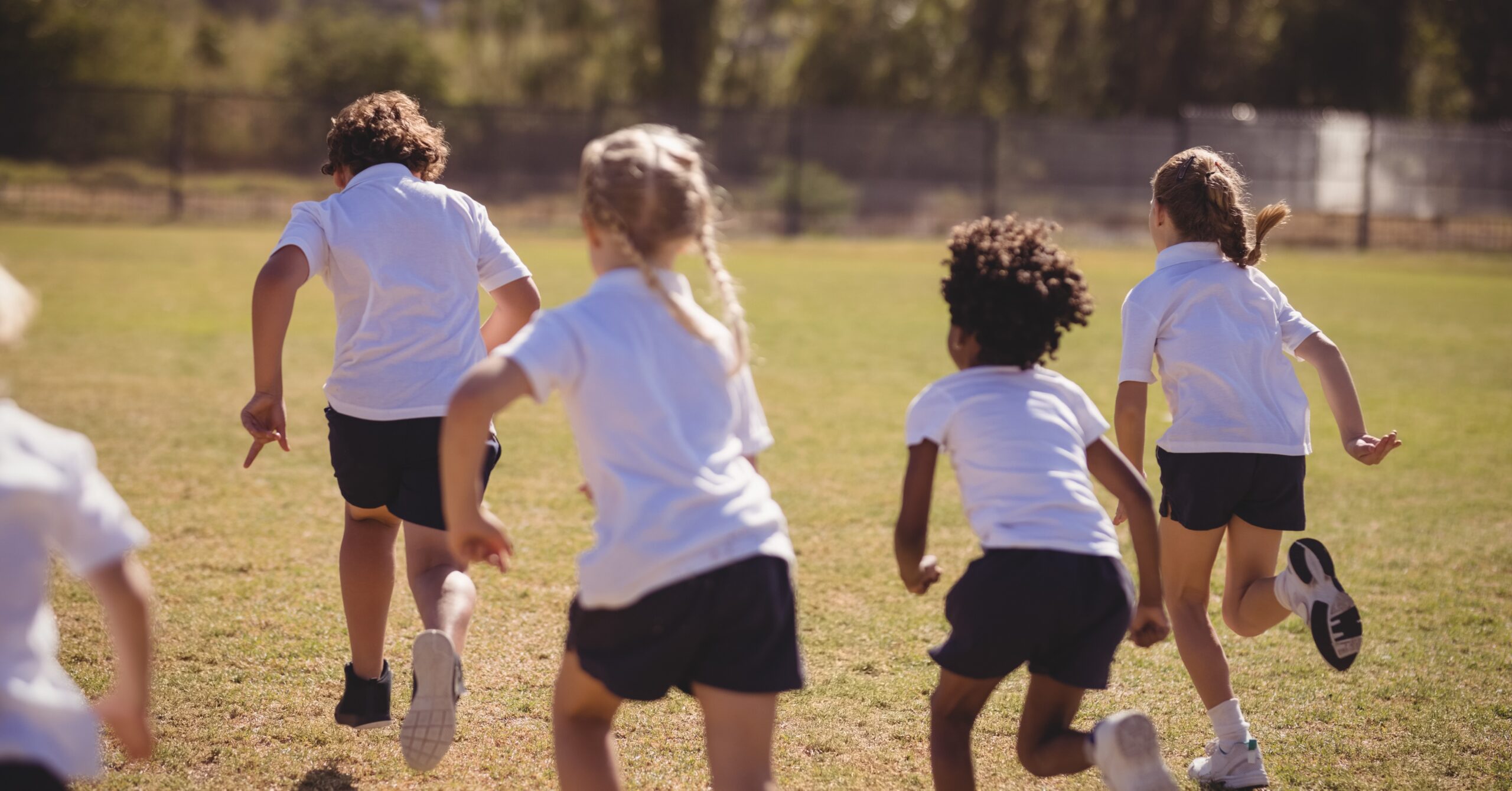 Young children in primary school running on a field to exercise.